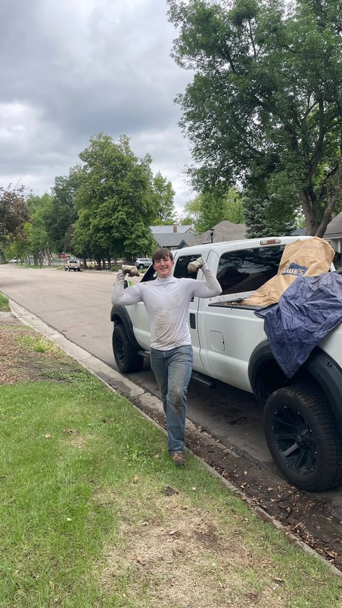 Man loading cargo into white pickup truck bed on residential street lined with trees