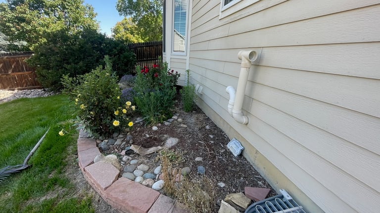 Side yard of house with landscaped flower bed, mulch, decorative stones, and green lawn under sunny sky