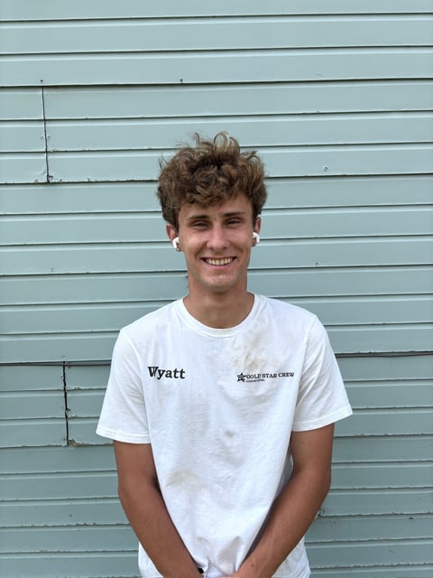 Young man named Wyatt smiling at camera wearing white t-shirt against light blue horizontal siding wall