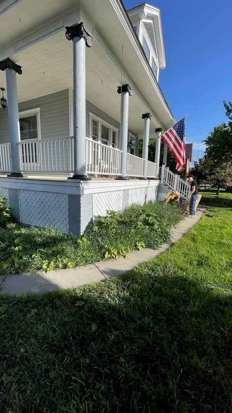 White farmhouse porch with columns and American flag, green lawn in foreground