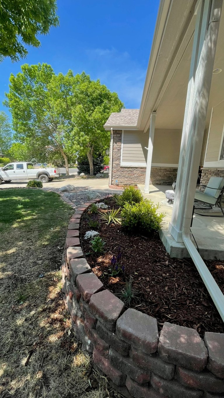 Front of house with landscaped flower bed, brick border, and driveway with white truck visible under trees