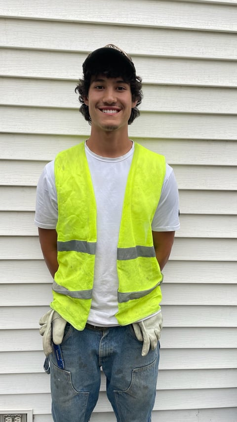 Young man wearing a neon yellow safety vest and work gloves standing in front of a white siding wall