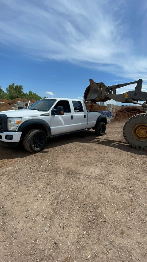 White Ford pickup truck parked next to a heavy equipment loader at a construction or gravel yard site