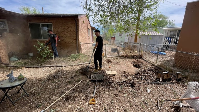 Two people working in a backyard with soil, measuring tape, and construction materials visible in a residential garden area