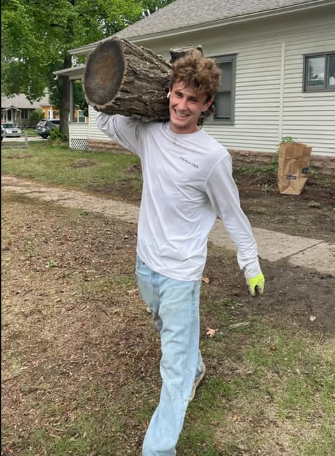 Man carrying large log on shoulder in front of residential house